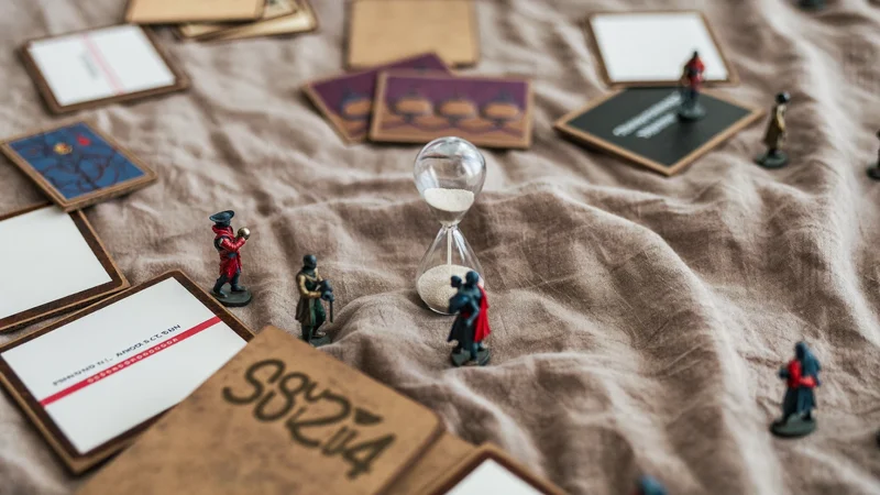 Gioco di carte cooperativo con miniature dipinte e clessidra su tovaglia di lino