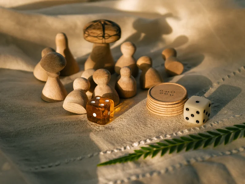 Dettaglio artigianale di meeple in legno, dadi levigati e segnalini di cartone su lino
